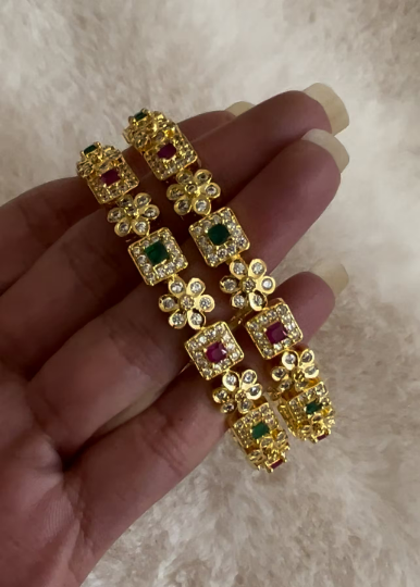 Gold bangle adorned with Ruby and Emerald gemstones.